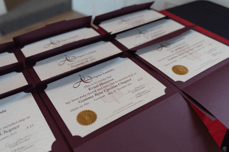 Close-up of several certificates in maroon folders on a table, featuring gold seals and the words Lambda Sigma Lambda with text about granting official membership.