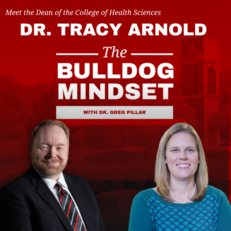 Two people in business attire pose in front of a red background with white text that reads: Dr. Tracy Arnold, The Bulldog Mindset with Dr. Greg Pillar. The background includes a faint campus building image.